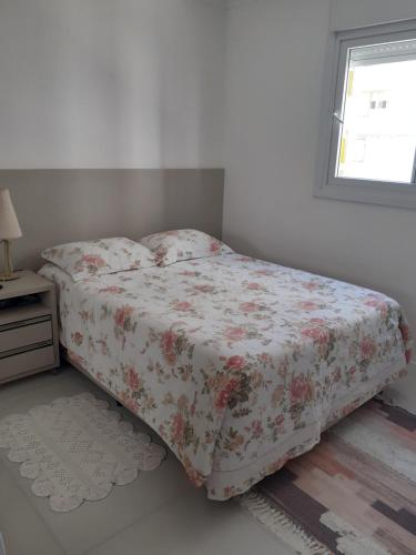 1 dormitorio con 1 cama con colcha de flores y ventana en Apartamento Encantador 250 metros do mar!, en Florianópolis