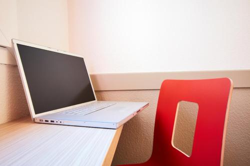 a laptop computer sitting on a desk next to a red chair at Première Classe Paris Ouest - Pont de Suresnes in Suresnes