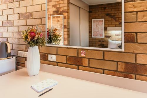 a vase of flowers on a table in front of a brick wall at Abacus Motel in Mount Isa