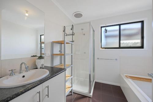 La salle de bains blanche est pourvue d'un lavabo et d'une douche. dans l'établissement Fontana Family Getaway WiFi, à Inverloch