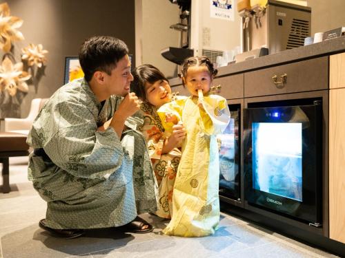 a man and two girls looking at a child in front of a microwave at Grandvrio Hotel Beppuwan Wakura - ROUTE INN HOTELS - in Beppu
