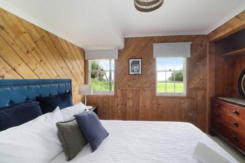 a bedroom with a bed with a blue headboard and two windows at White Shell Cottage - Woodfire & Beachfront in Falmouth
