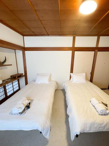 two beds in a room with white sheets at Kikusui Ryokan in Tamano