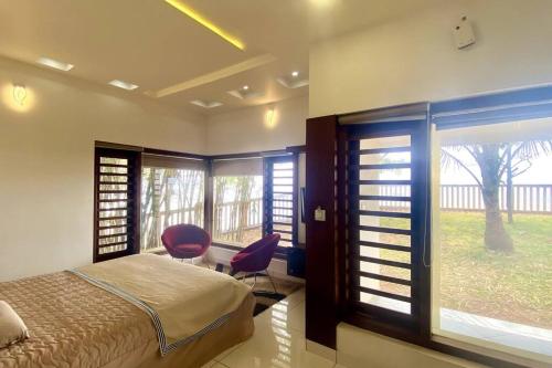 a bedroom with a bed and two chairs and windows at Willo Stays Sea View Home Kannur Landsend in Kannur