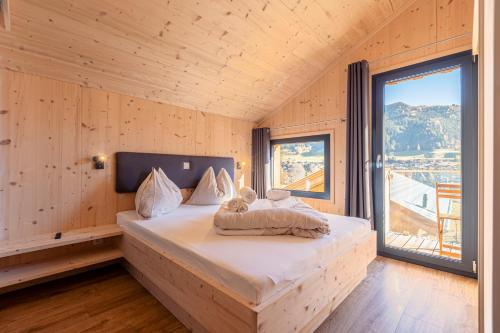 a bed in a wooden room with a large window at Bergeralm Chalets by ALPS RESORTS in Steinach am Brenner