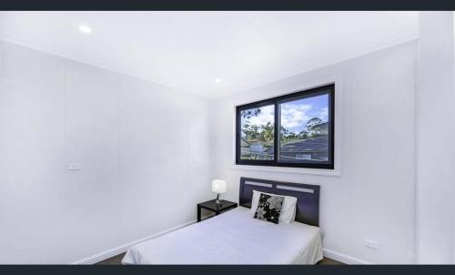 een witte kamer met een bed en een raam bij New Gymea House in Gymea