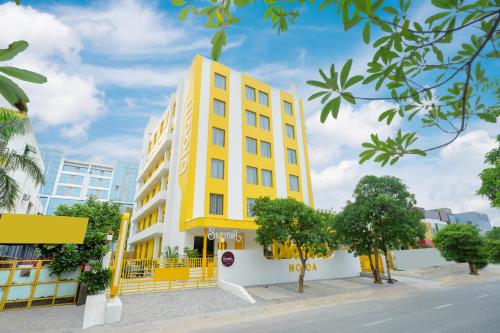 a yellow building with trees in front of a street at Bloom Hotel - Sector 62 in Noida