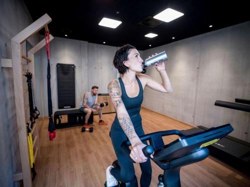 a woman standing on a treadmill drinking from a hair dryer at All-Suite Resort Fieberbrunn inklusive Gästekarte & Aubad-Eintritt in Fieberbrunn