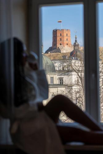 a woman sitting on a window sill looking at a castle at Grand Hotel Vilnius, Curio Collection by Hilton in Vilnius