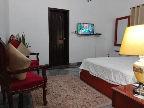 a bedroom with a bed and a chair and a tv at Homewood Suites Family Guest House & Apartments in Lahore