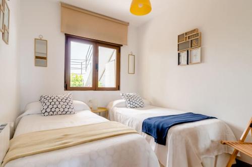 2 camas en una habitación con paredes blancas y ventana en Casa de Las Flores - Apartamento con jardín privado frente a la Playa de Comillas, en Comillas