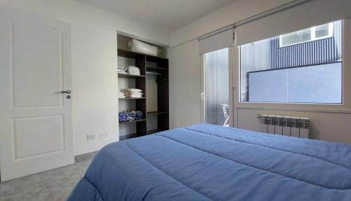 1 dormitorio con cama azul y ventana grande en Departamento con vista al lago y cerros en San Carlos de Bariloche