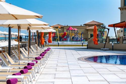 a row of lounge chairs with umbrellas and a pool at The Grove Resort Bahrain in Manama