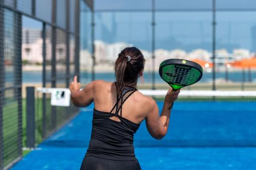 a woman holding a tennis racquet on a tennis court at The Grove Resort Bahrain in Manama