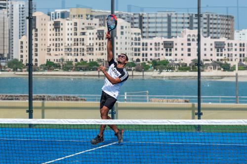 a man jumping to hit a tennis ball with a racket at The Grove Resort Bahrain in Manama