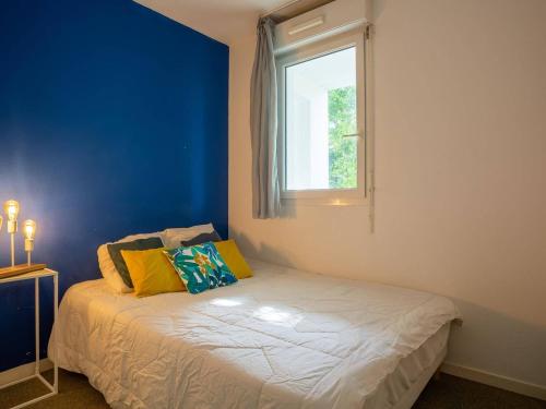 Cet appartement comprend une chambre dotée d'un lit avec un mur bleu et une fenêtre. dans l'établissement Aperçu mer: Bel appartement avec piscine, tennis et proche plage - FR-1-3-450, à Bidart