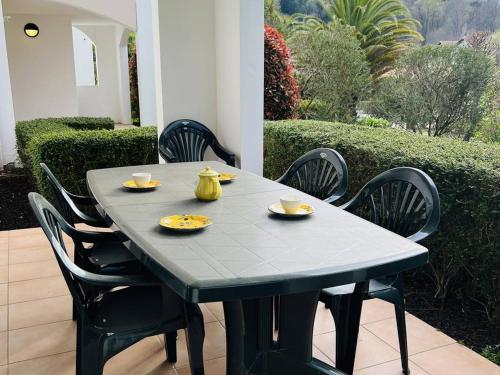 - une table noire avec des chaises et une table avec des plats jaunes dans l'établissement Appartement T3 avec Terrasse et Piscine, 4 Couchages, Proche Centre-Ville - Cambo-les-Bains - FR-1-495-18, à Cambo-les-Bains