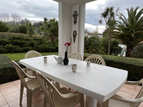 une table blanche avec des chaises et un vase avec des fleurs dans l'établissement Cambo-les-Bains: T3 Moderne avec Terrasse, Parc, Piscine, Parking, et Internet - 4 Couchages - FR-1-495-20, à Cambo-les-Bains