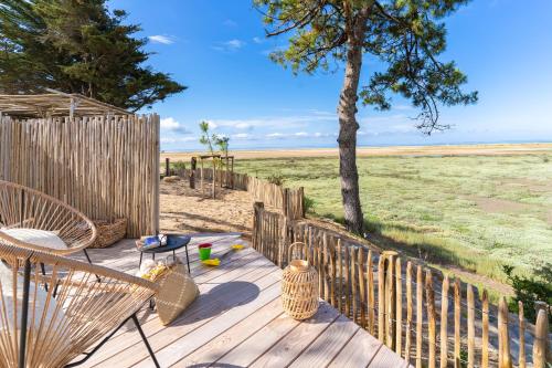una terrazza in legno con sedie, un albero e un campo di Camping Le Bellevue a La Tranche-sur-Mer