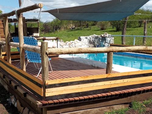 a deck with a chair and an umbrella next to a pool at Cabañas Buen Ayre in Villa Rumipal