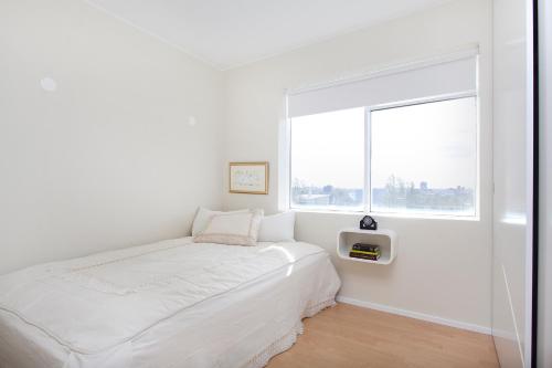 a white bedroom with a bed and a window at Overlooking the city, bright & cozy - Free Parking (A2) in Reykjavík