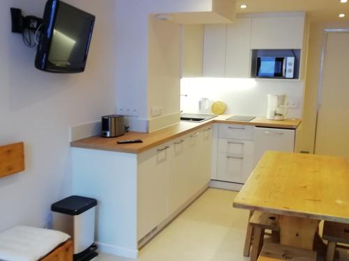 une cuisine avec des armoires blanches et une table en bois dans l'établissement Duplex 2 pièces - 5 pers, balcon au sud, skis aux pieds, à 3 min du Transarc, village Charmettoger - FR-1-411-831, à Bourg-Saint-Maurice