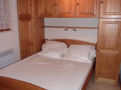 - un lit avec 2 oreillers blancs et des placards en bois dans l'établissement Appartement cosy 6 pers. proche pistes avec balcon, casier à skis et parking couvert - FR-1-573-32, à Saint-Jean-dʼAulps