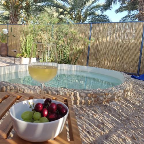 a bowl of fruit and a glass of wine next to a swimming pool at אתיטיוד בערבה attitude at the arava in H̱aẕeva