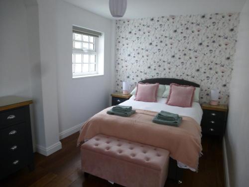um quarto com uma cama com almofadas cor-de-rosa e uma janela em Delfryn Holiday Cottage em Colwyn Bay