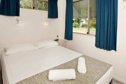 a bedroom with a bed with blue curtains and a window at Ellis Beach Oceanfront Holiday Park in Palm Cove