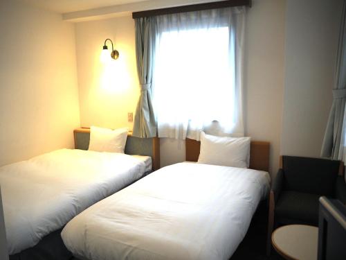 two beds in a hotel room with a window at Hotel Green Mark in Sendai