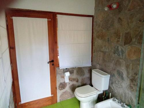 baño con aseo blanco y pared de piedra en Loft on Los Reartes River, Intiyaco en Villa Berna
