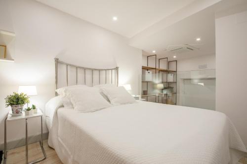a white bedroom with a large bed with white sheets at Loft duplex Sevilla wall in Seville