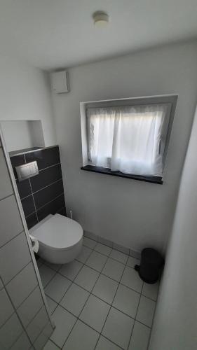 a white bathroom with a toilet and a window at Reetdachhaus Moordeichperle in Nordstrand