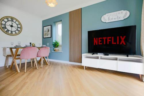 a living room with a television and a table with pink chairs at Middleton House with Free Parking, Fast-Wifi, SmartTV and Garden by Yoko Property in Milton Keynes