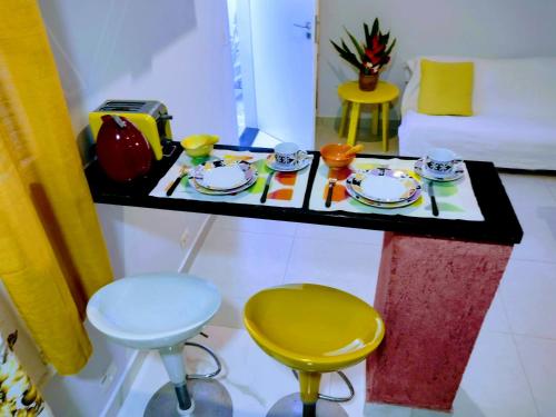 una mesa con platos, tazas y sillas en una habitación en Flat Ideal Guarujá - Apto Studio Mobiliado, Ar-Condic e Cozinha Completa en Guarujá