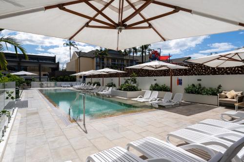 uma piscina com cadeiras brancas e guarda-sóis em Ruby Gold Coast By Serain em Gold Coast