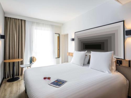um quarto de hotel com uma cama branca com um livro em ibis Brest Centre em Brest