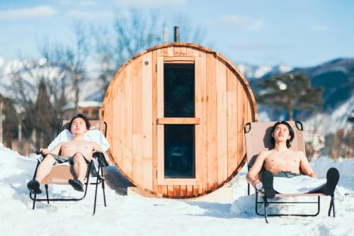 two men sitting in chairs in the snow in front of a sauna at From P in Hakuba