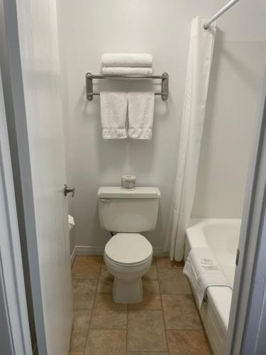 a bathroom with a white toilet and a tub and towels at Anavada Inn & Suites - Grande Prairie in Grande Prairie