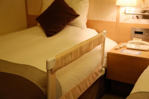 a bed in a hotel room with a phone on a table at Hotel Monterey Grasmere Osaka in Osaka