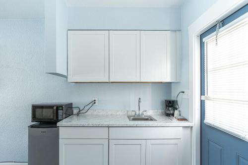 a kitchen with white cabinets and a sink and a microwave at Echo Sails Motel in Clearwater Beach