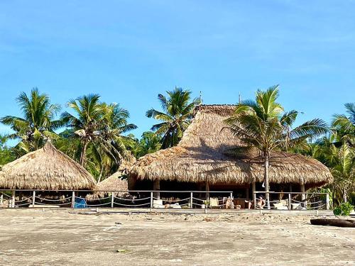 a group of straw huts on a beach with palm trees at Sumba Beach House in Waikabubak