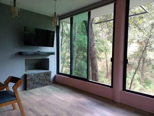 ein Wohnzimmer mit großen Fenstern und einem TV in der Unterkunft Cabaña Nala de lujo para parejas in Mazamitla