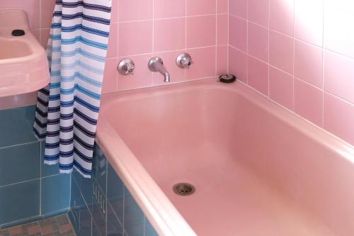 una vasca rosa in un bagno piastrellato rosa di Hoopers Cottage ad Aldgate