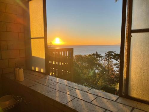 a view of the ocean from a window with the sunset at 伊豆稲取テラス-寛道- in Shimoda