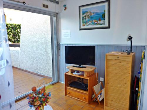 un salon avec une télévision à écran plat et une table dans l'établissement Appartement Rez-de-Jardin: Piscine, Terrasse, Parking, Wi-Fi en Option - FR-1-387-63, à Marseillan