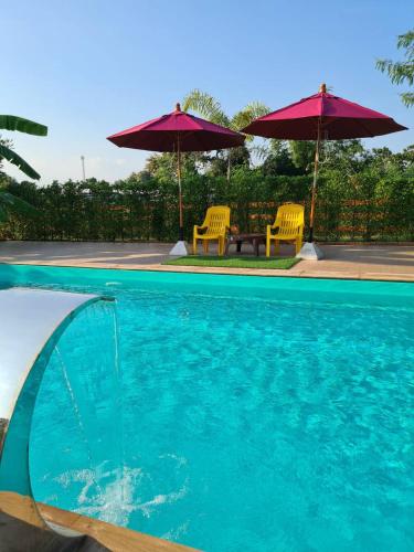 a swimming pool with two chairs and umbrellas at Lampang Hideaway Guesthouse in Lampang