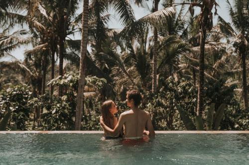 a man and a woman sitting in a swimming pool at Kusfarm Bali in Selemadeg