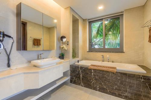 a bathroom with a tub and a sink and a mirror at The Ocean Villa Resort Beachfront By Abogo in Da Nang